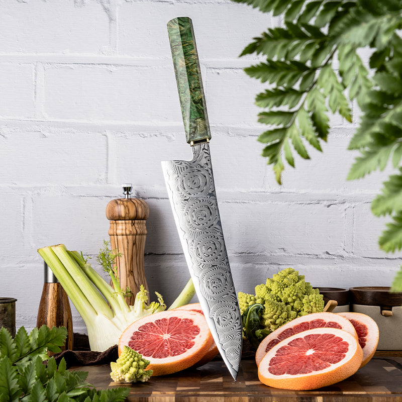 Cuchillo de Chef 22cm 10Cr+Rosa Damasco66 Madera EST Verde y Cobre, sobre una tabla de picar, acompañado de naranjas.