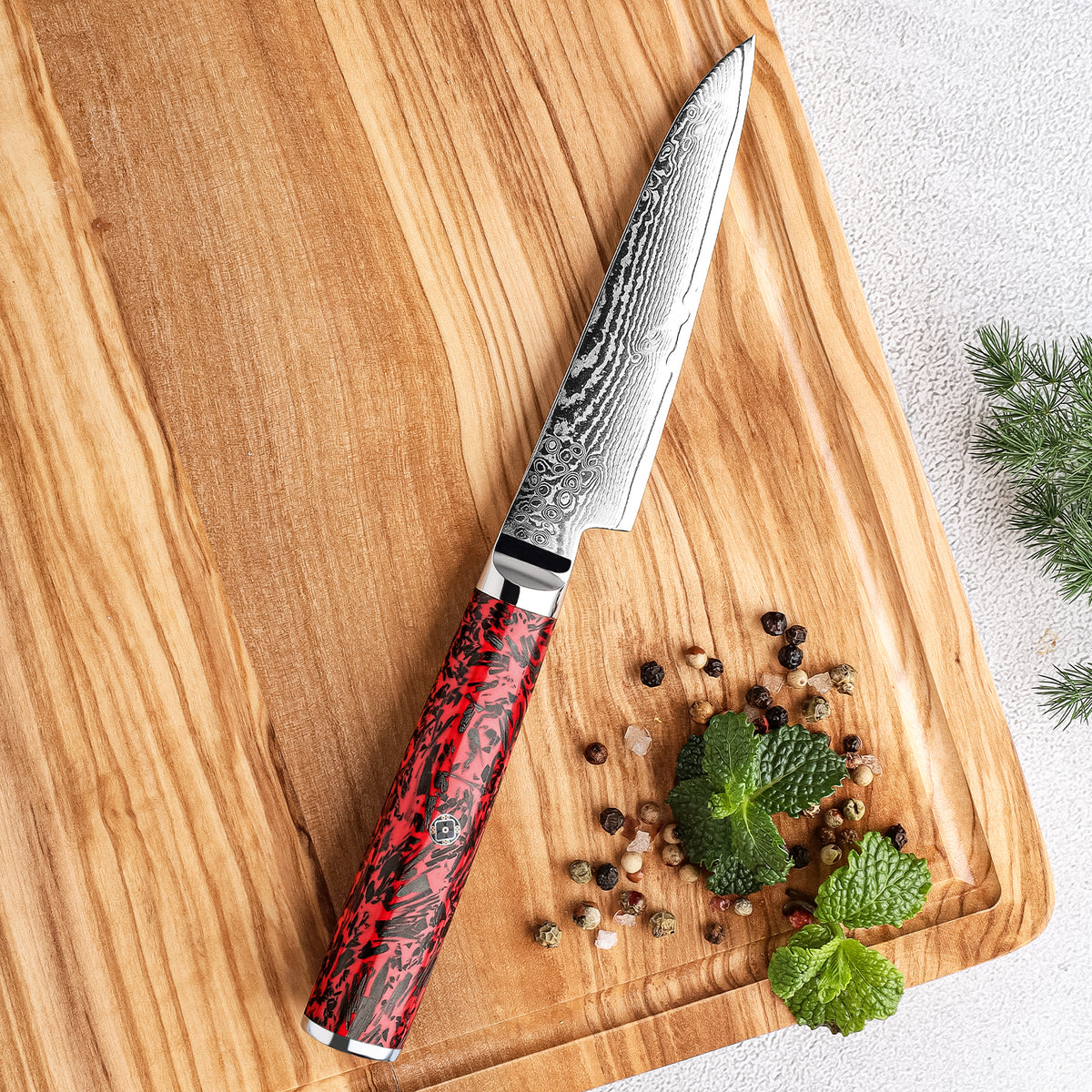Cuchillo Puntilla 10cm S35VN+Ola Damasco66 Resina Roja y Carbono sobre tabla con lindas vetas de madera acompañada pimienta roja y hierbas aromáticas menta cilantro