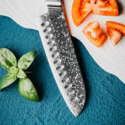 Cuchillo Santoku 18cm 10Cr+Gotas Damasco128 Full Tang Resina Azul, compañado de tomate y estrella de hojas de albaca.
