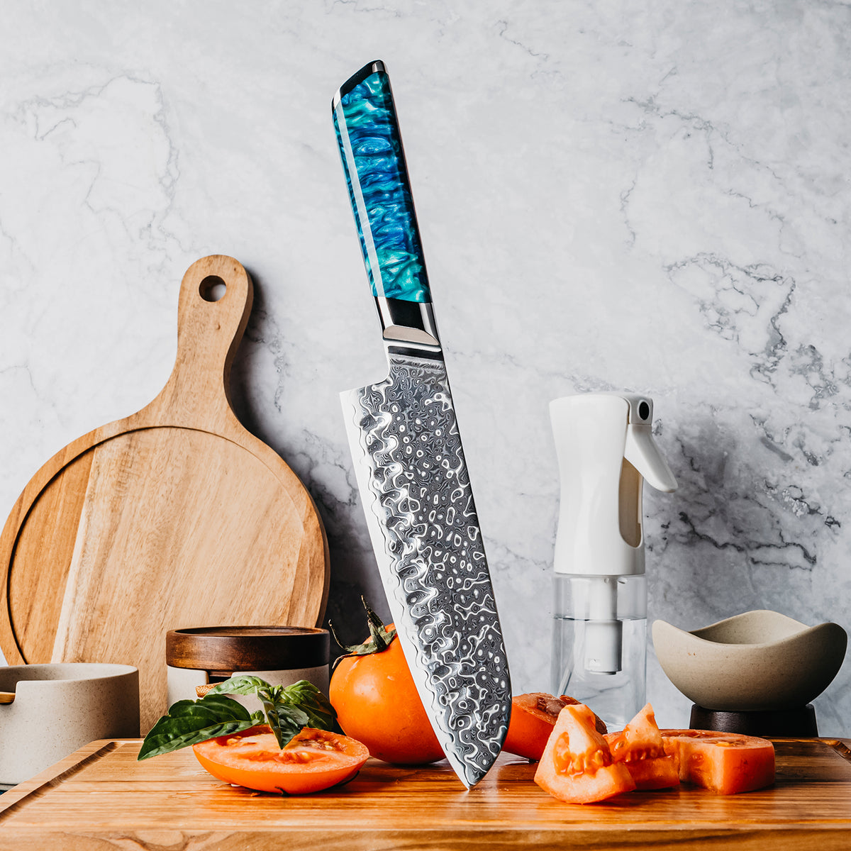 Cuchillo Santoku 18cm 10Cr+Gotas Damasco128 Full Tang Resina Azul, sobre tabla de picar, acompañado de tomate.
