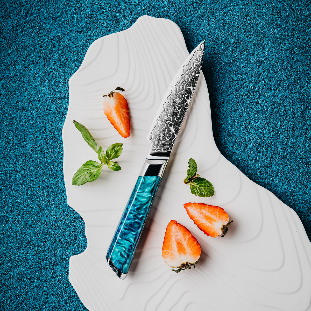 Cuchillo Puntilla 10cm 10Cr+Gotas Damasco128 Full Tang Resina Azul cuchillo centrado. acompñado de frutas.