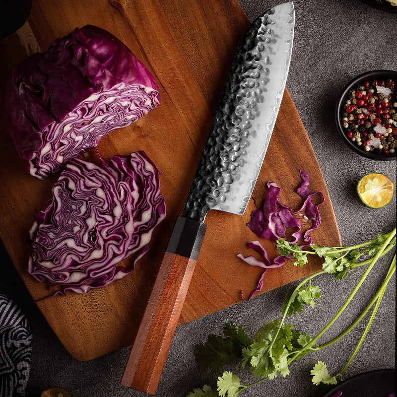 Cuchillo Santoku 19cm AUS-10 Clad Kurouchi Martillado Mango Mkuruti y Ebano, sobre tabla de picar, acompañado kol rojo y cilantro