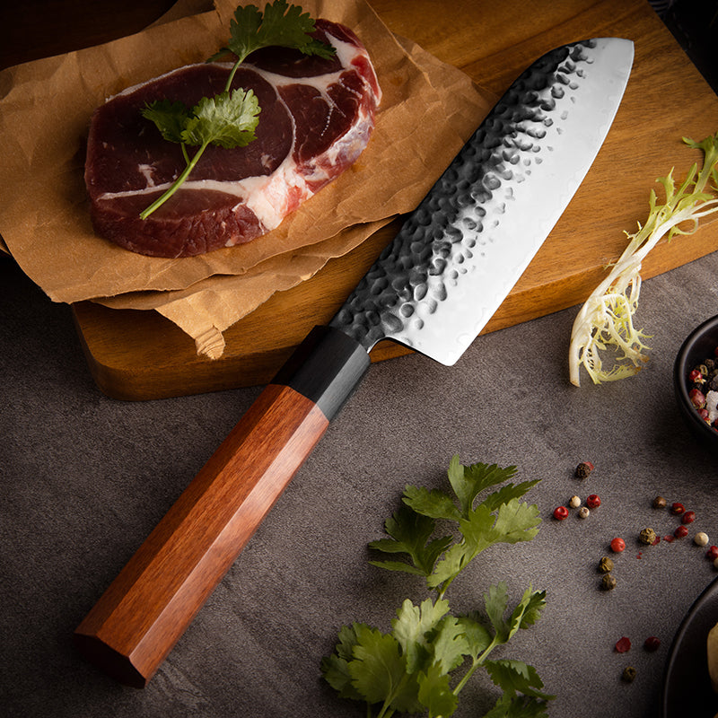Cuchillo Santoku 19cm AUS-10 Clad Kurouchi Martillado Mango Mkuruti y Ebano, sobre tabla de picar, acompañado con carne de rez