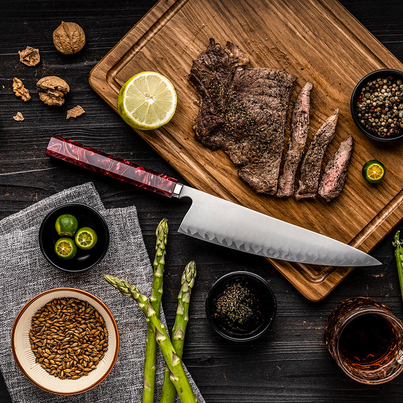Vista cenital del cuchillo de chef HM-59A de 21 cm junto a carne asada, espárragos y limón.